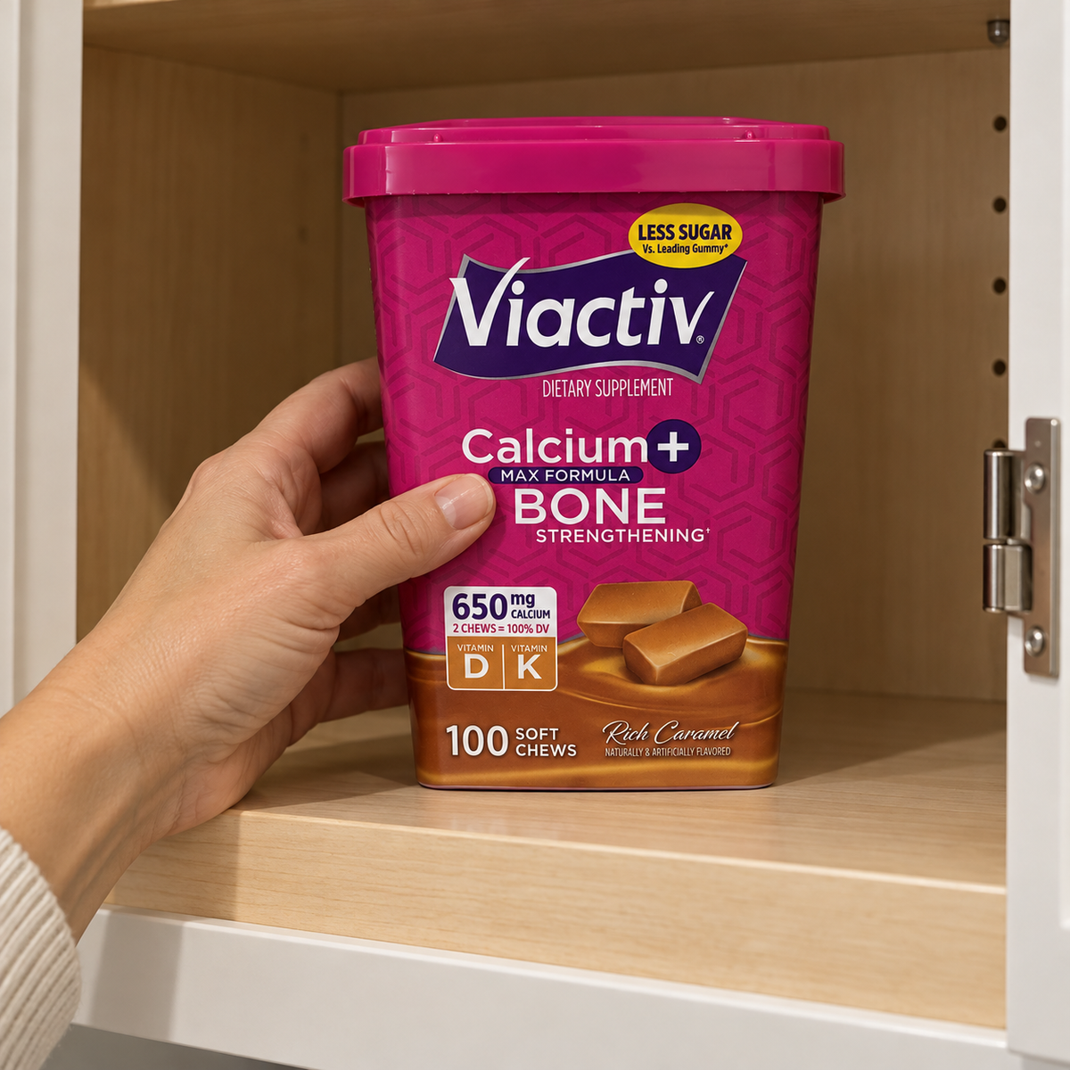 A hand placing a closed Viactiv Rich Caramel 100-chew container on a cupboard shelf.