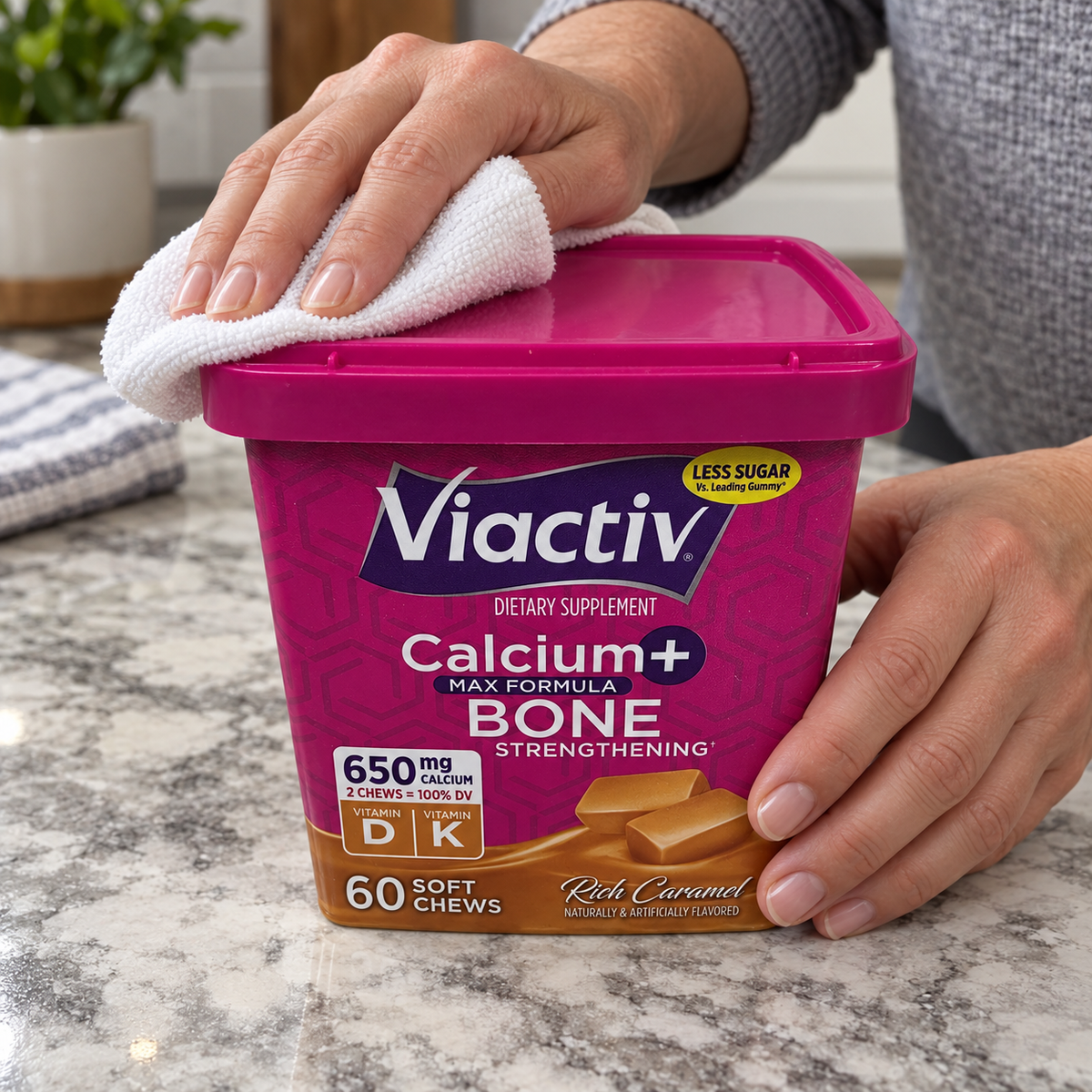 Hands wiping the closed lid of a Viactiv Rich Caramel 60-chew container with a cloth.